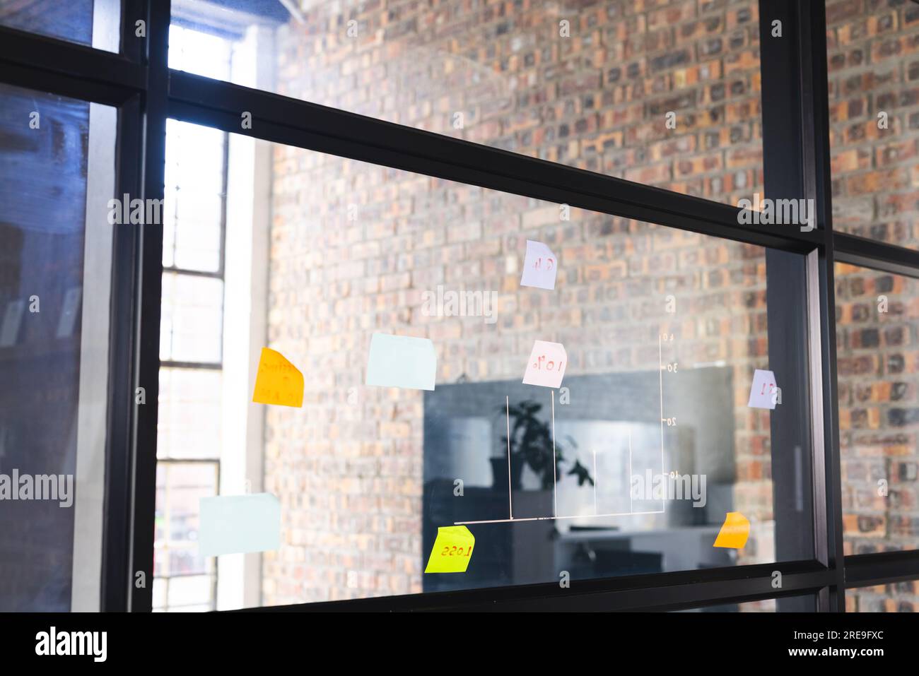 Glaswand mit bunten Noten über Backsteinwand mit großem schwarzem Bildschirm im Büro Stockfoto