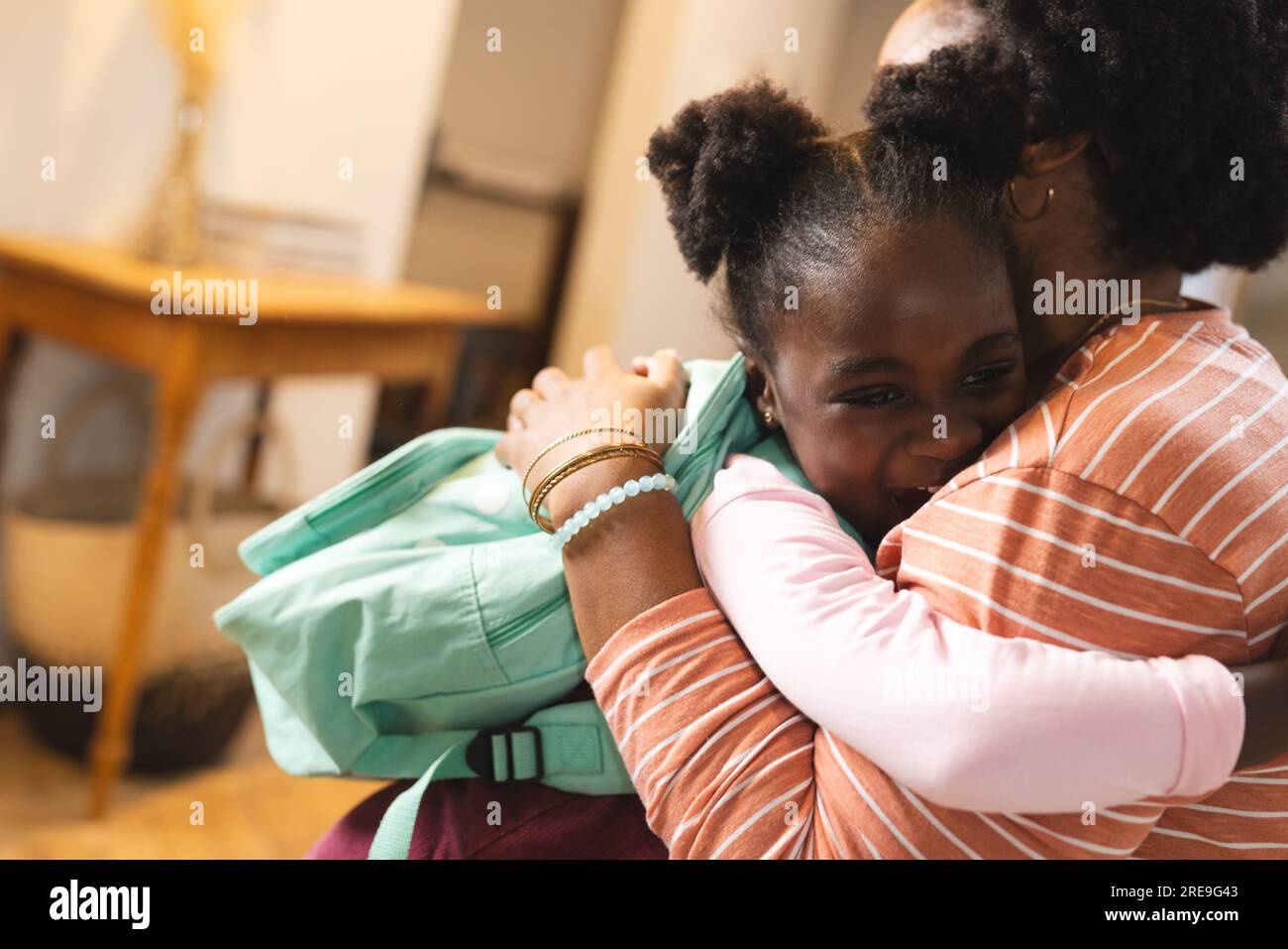 Glückliche afroamerikanische Mutter und Tochter, die sich vor der Schule zu Hause umarmen Stockfoto