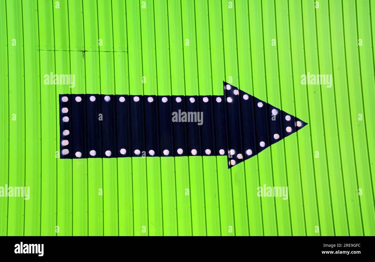 Die neongrüne Wand hat einen schwarzen Pfeil, der in die Richtung weist. Der Pfeil ist mit weißen Punkten markiert. Stockfoto