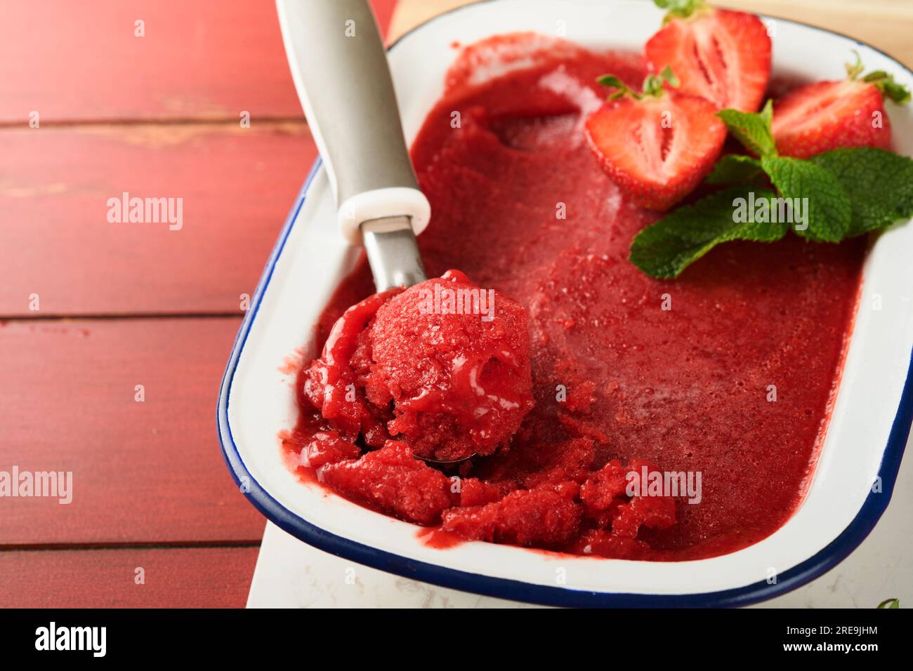 Erdbeer-Granita oder frisches Beerensorbet in weißer rustikaler Schüssel auf altem Holztisch. Eis mit Erdbeere und Minze. Sommervergnügen. Oben vi Stockfoto