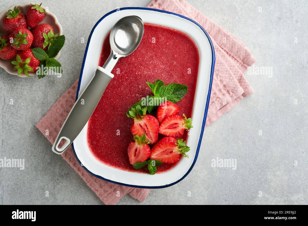 Erdbeer-Granita oder frisches Beerensorbet in weißer rustikaler Schüssel auf grauem Betonhintergrund. Eis mit Erdbeere und Minze. Sommervergnügen. Draufsicht. Stockfoto