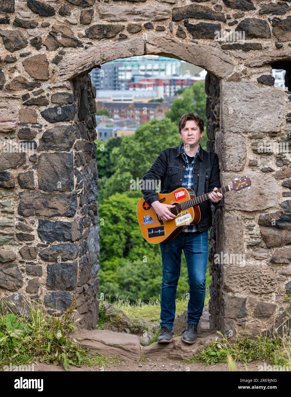 Der einsame Musiker Mike Baillie spielt Gitarre in den Ruinen der St. Anthony's Chapel, Holyrood Park, Edinburgh, Cotland, Großbritannien Stockfoto