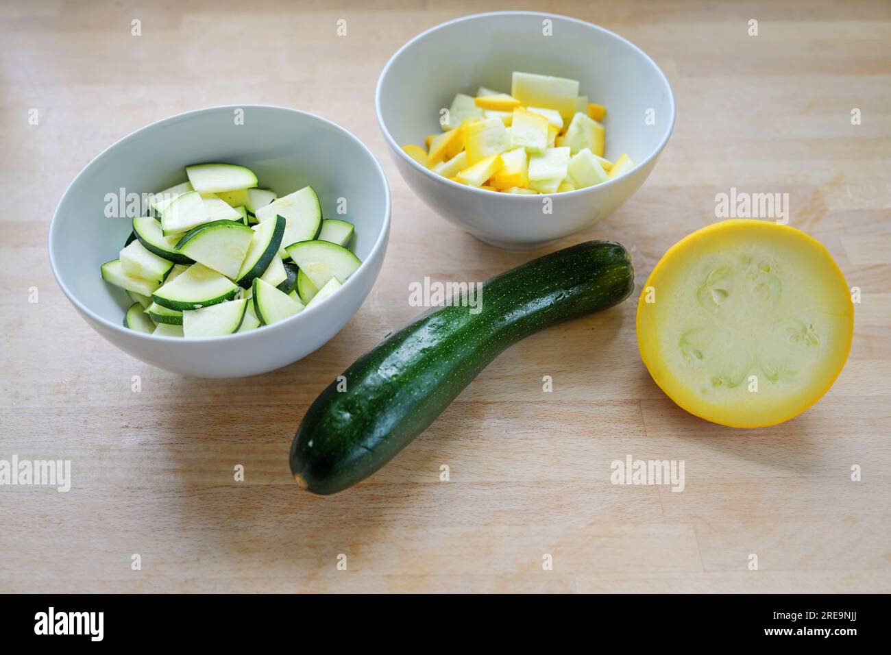 Grüne und gelbe Zucchini, ganz und gehackt in einer Schüssel, Zutat für verschiedene Gemüsegerichte auf einem hölzernen Küchenbrett, vegetarisches Kochkonzept, Stockfoto