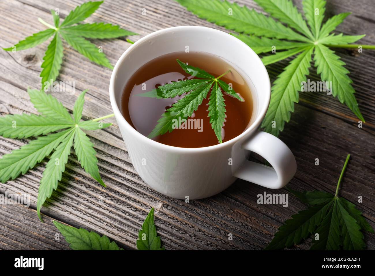 Tee mit Cannabisblättern auf einem Holztisch. Medizinischer Kräutertee mit Marihuana aus der Nähe Stockfoto