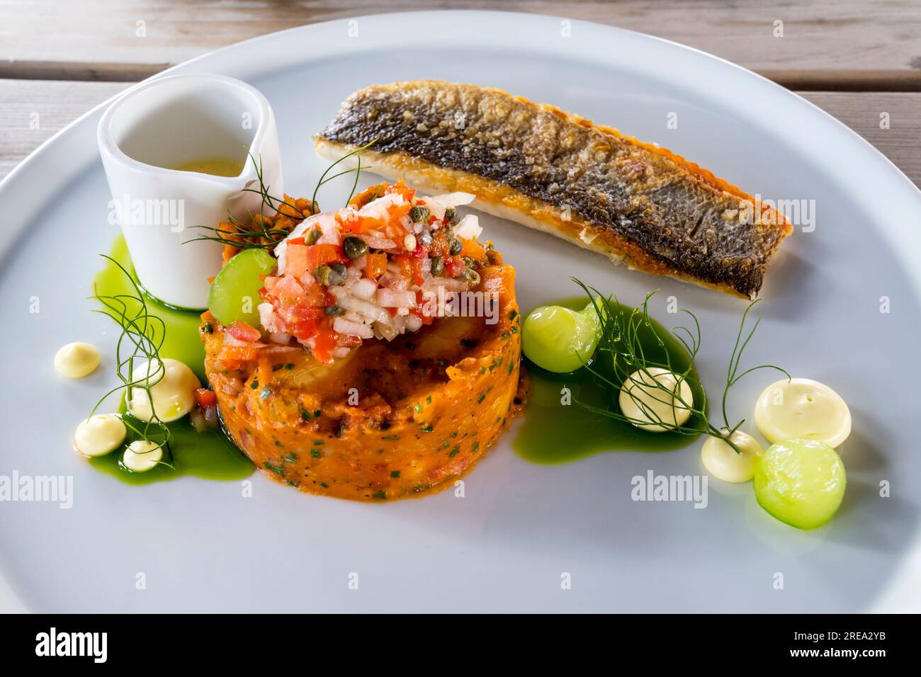 Eine Gastropub-Mahlzeit mit Seebarschfilet mit Chorizo und Patatas bravas und eingelegter Gurkensalsa. Stockfoto
