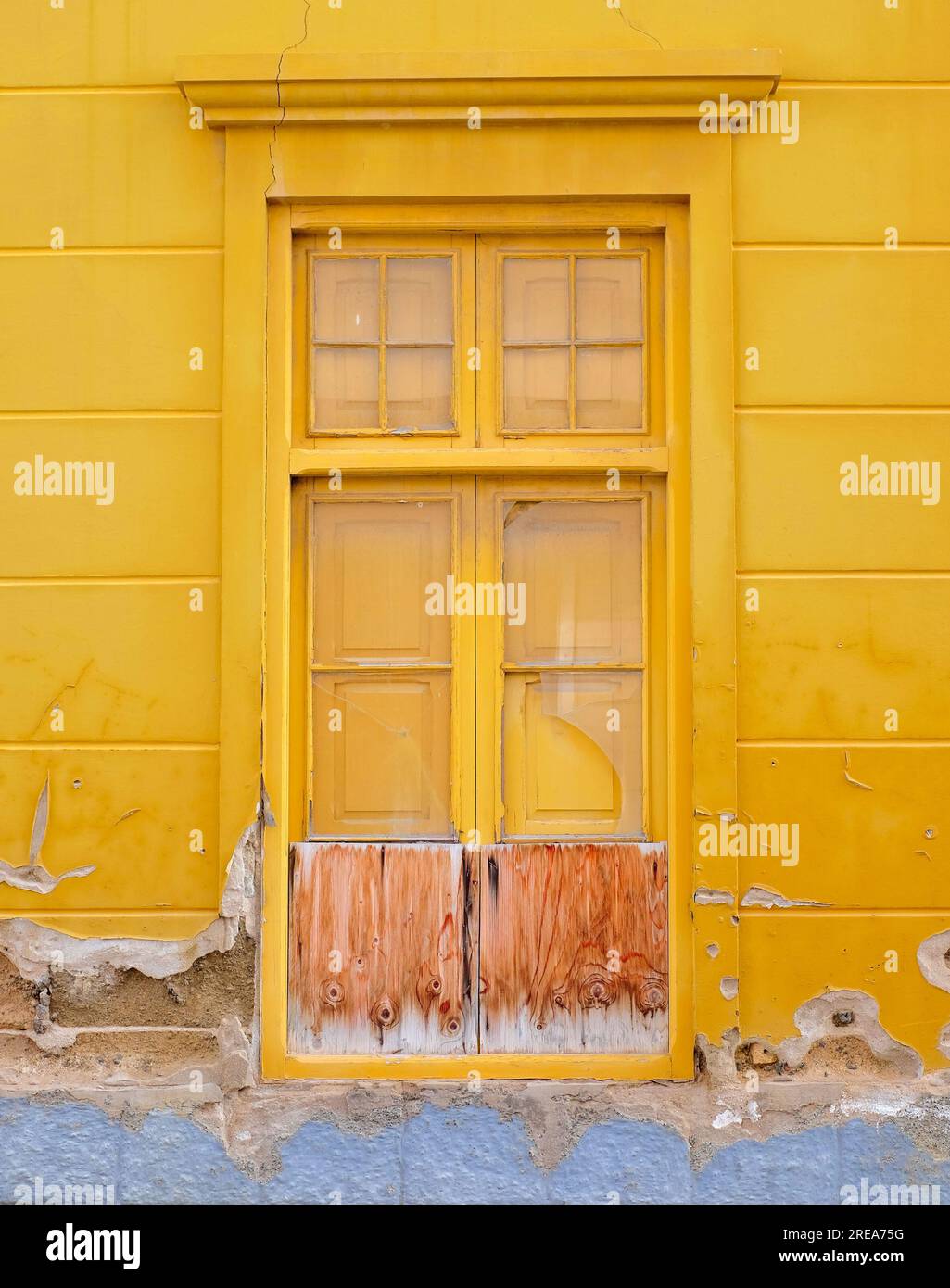 Ein einfacher Holzrahmen, ein altes Fenster in einer gelben Wand. Stockfoto