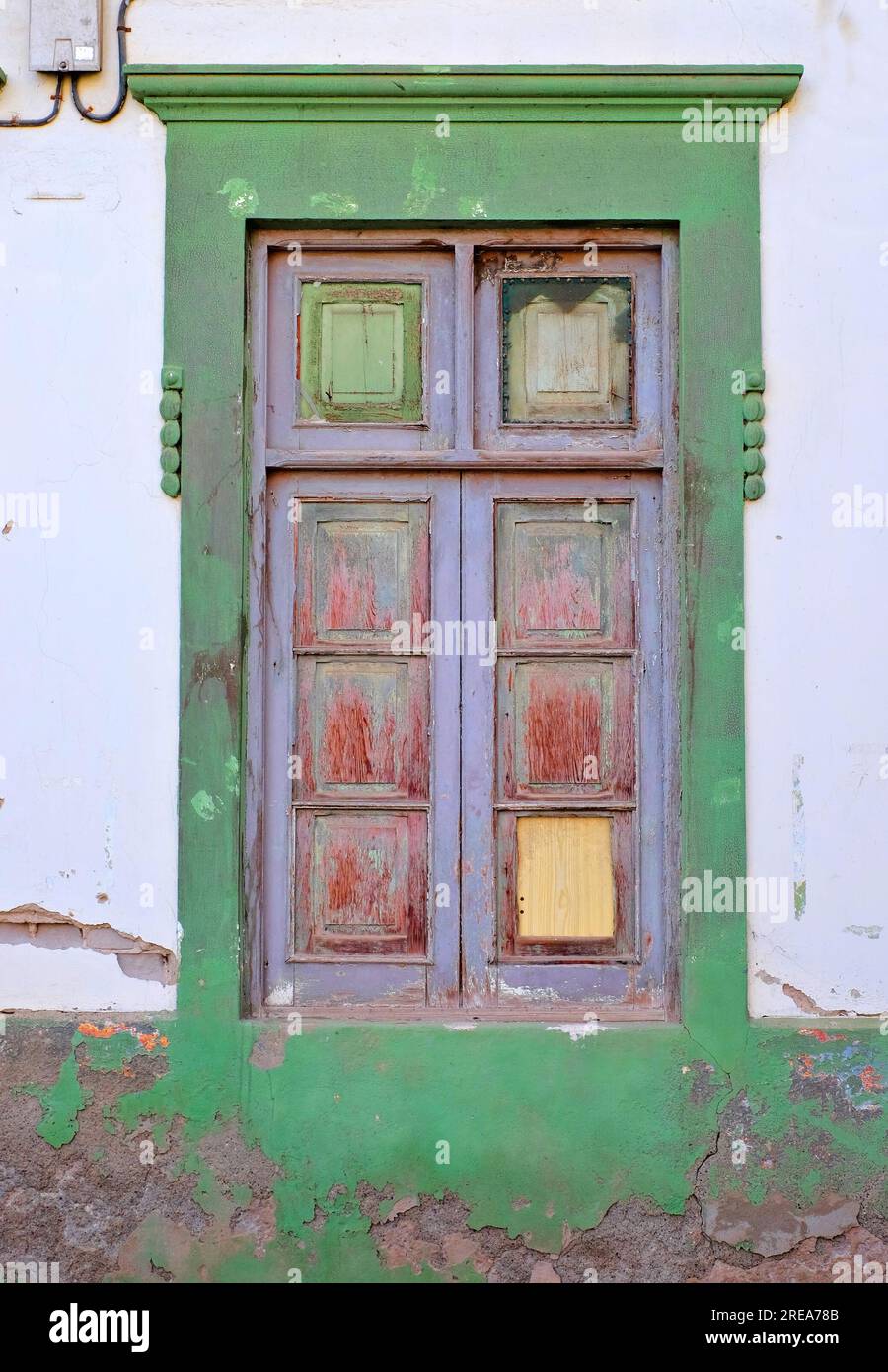 Ein einfacher Holzrahmen, grau gemalt, altes Fenster in einer grünen Wand. Stockfoto