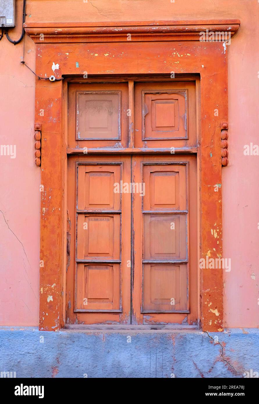 Ein einfaches geschlossenes altes Holzfenster in einer rot-rosa bemalten Wand. Stockfoto