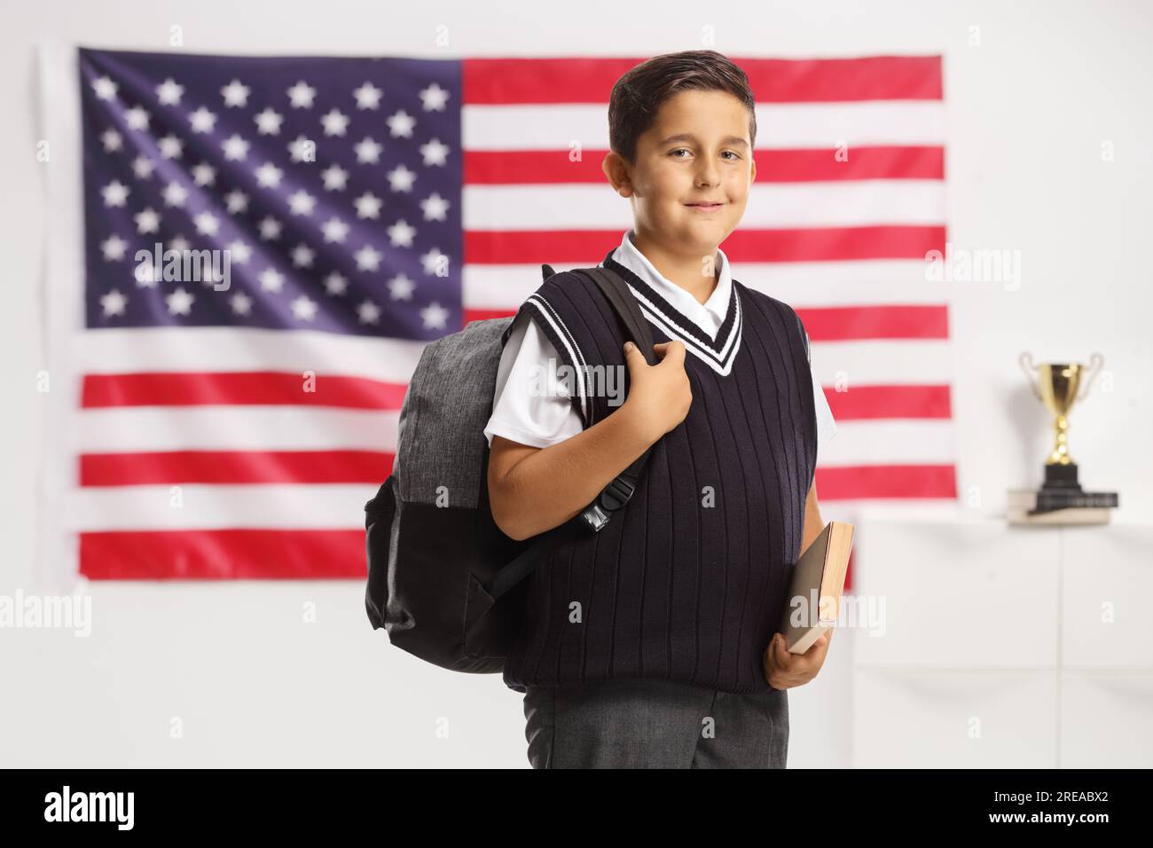 Schuluniform für Jungen mit einem Buch und einem Rucksack vor einer US-Flagge Stockfoto