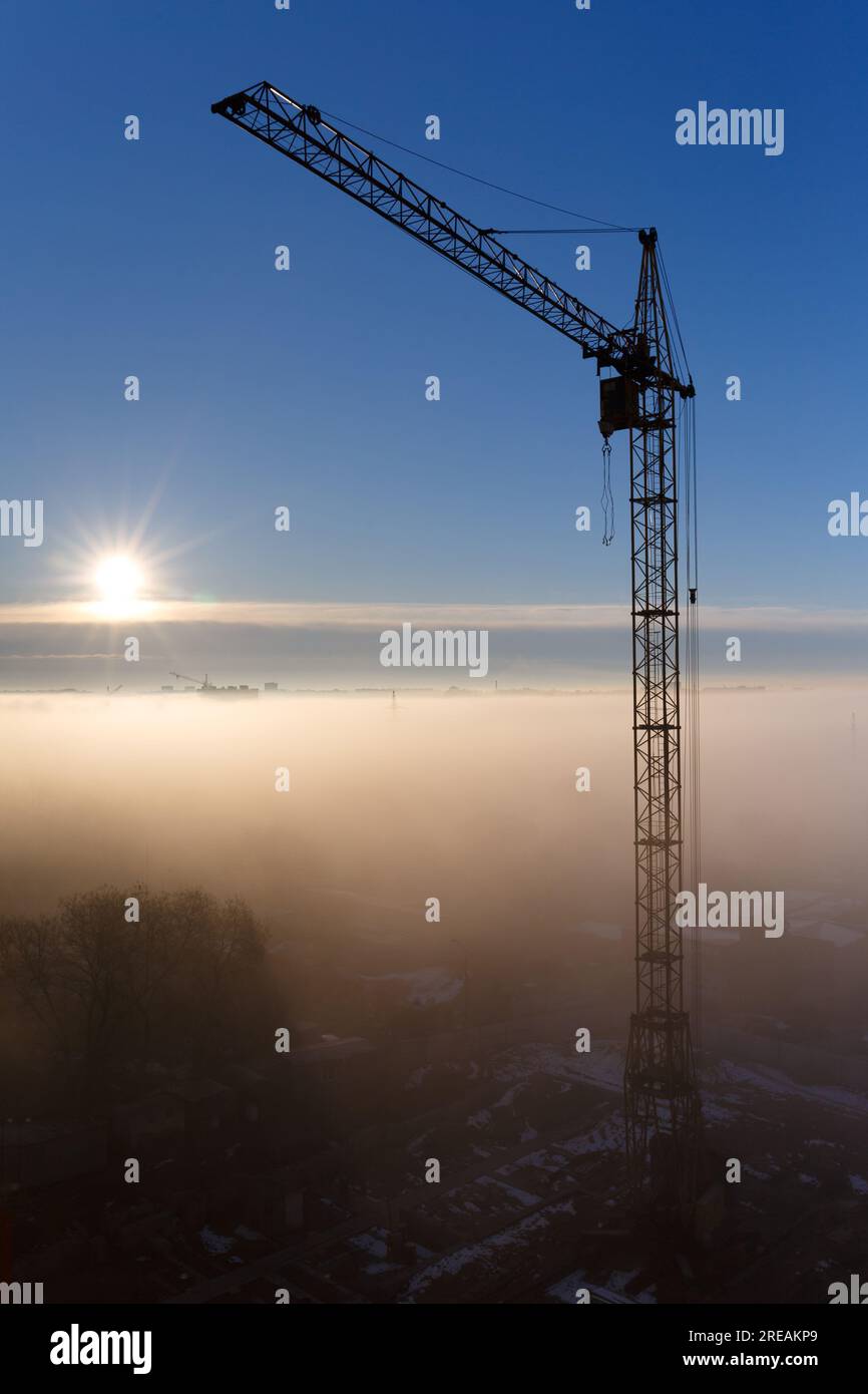 Baukran im Nebel am Morgen. Sonnenaufgang, Morgennebel, Baustelle, Turmkran. Mystischer nebliger Morgen in der Stadt bei Tagesanbruch. Stockfoto