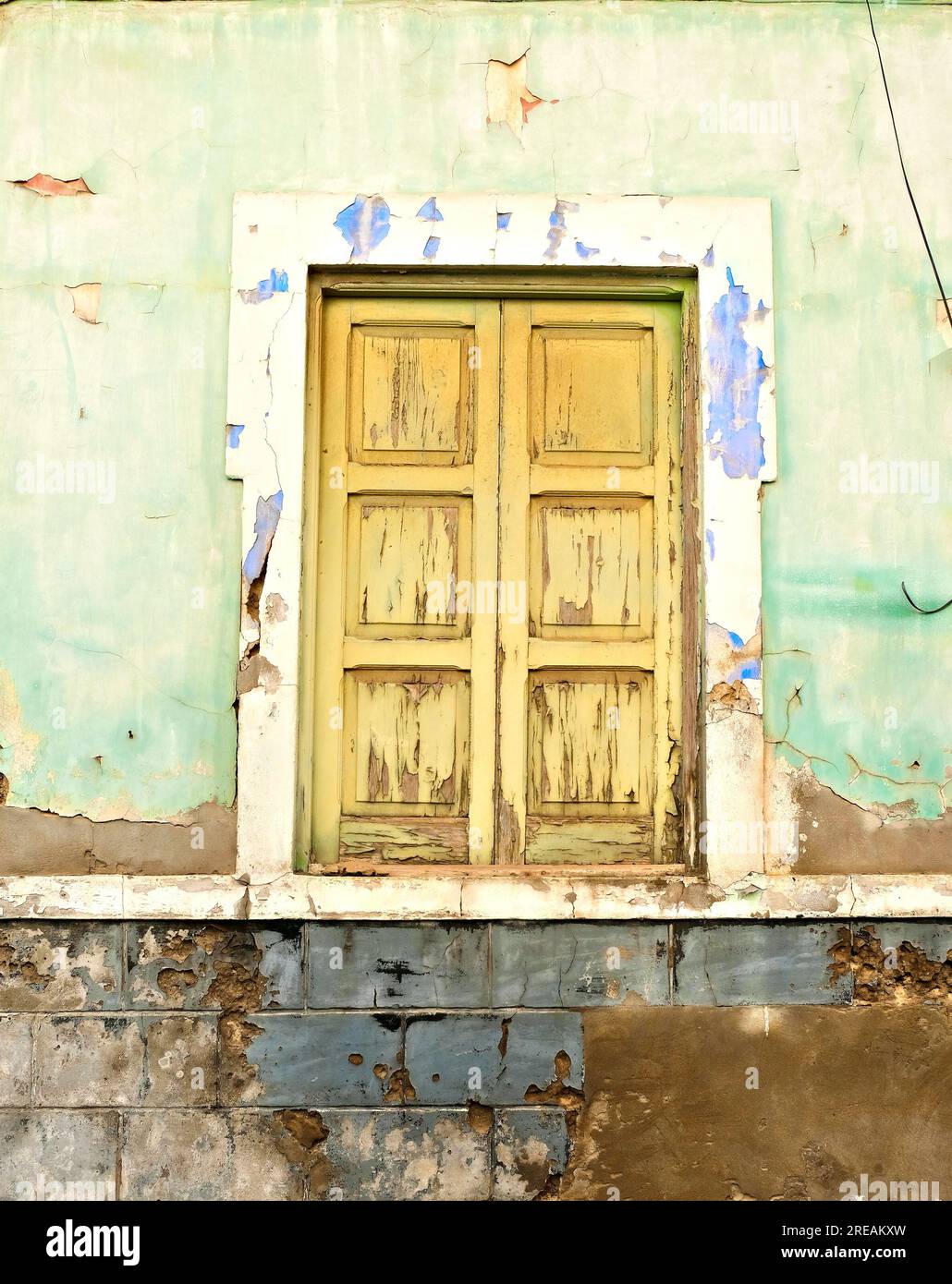 Ein einfaches altes Holzfenster in einer verwitterten, hellgrünen Wand mit abblätternder Farbe. Stockfoto