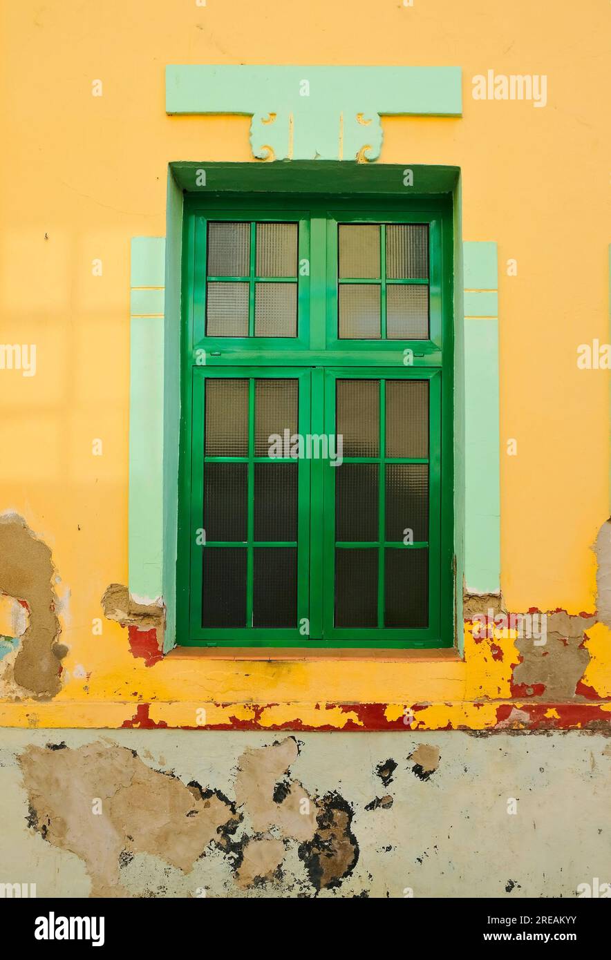 Ein einfaches, modernes Rahmenfenster aus Legierung in einer gereiften orangefarbenen Wand mit abblätternder Farbe. Stockfoto