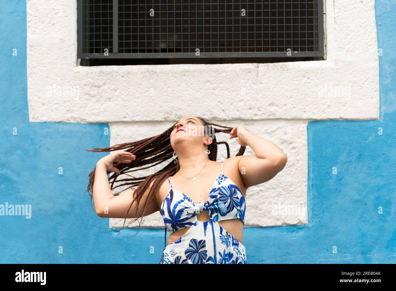 Eine hübsche Frau, die ihre Haare an die blaue Wand eines alten Hauses wirft. Pelourinho, Brasilien. Stockfoto