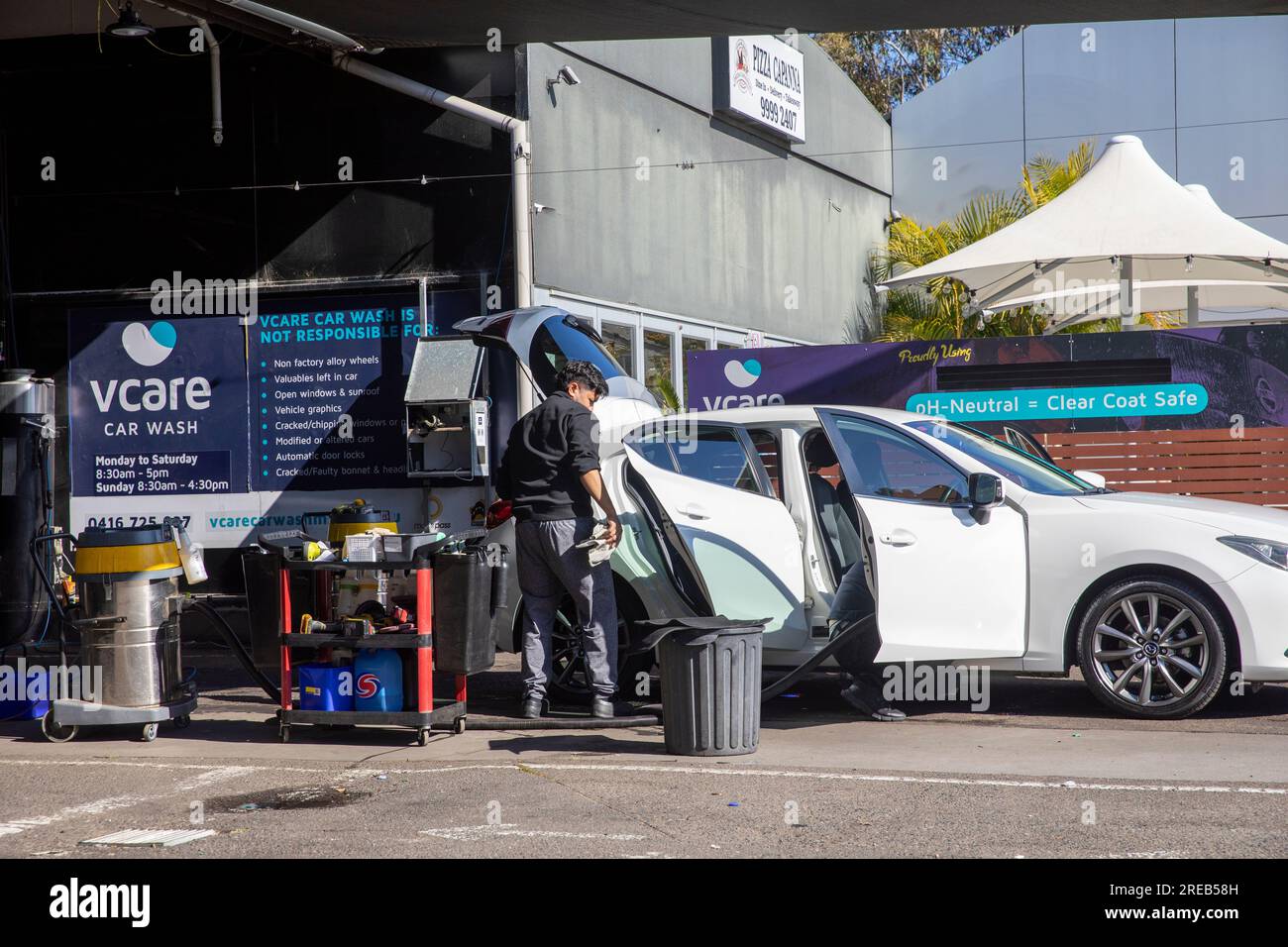 Handwaschservice in Sydney, Australien, Mitarbeiter bei Autowaschanlage reinigt ein weißes Auto mit offenen Türen, Australien, 2023 Stockfoto