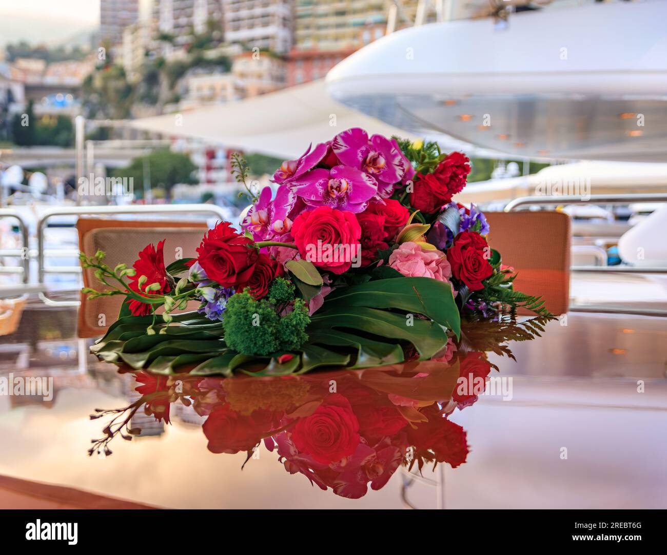 Wunderschöne, lebendige Blumenarrangements mit Orchideen und Rosen auf einer Luxusyacht mit verschwommenem Monte Carlo, Monaco Stadtbild im Hintergrund bei Sonnenuntergang Stockfoto