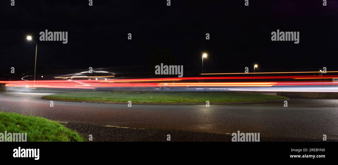 Fahrzeuge, die nachts in einem Kreisverkehr unterwegs sind und Lichtpfade hinterlassen, fotografiert mit Langzeitbelichtung. Stockfoto