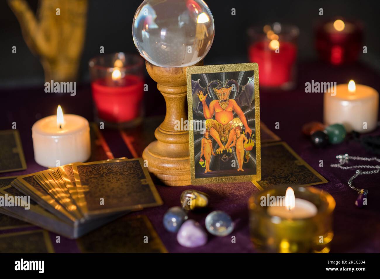Ein Set brennender Kerzen mit Teufelskarten und einer transparenten Glaskugel mit glatten bunten Steinen auf einem hölzernen Ständer auf dem Tisch des Wahrsagers Stockfoto