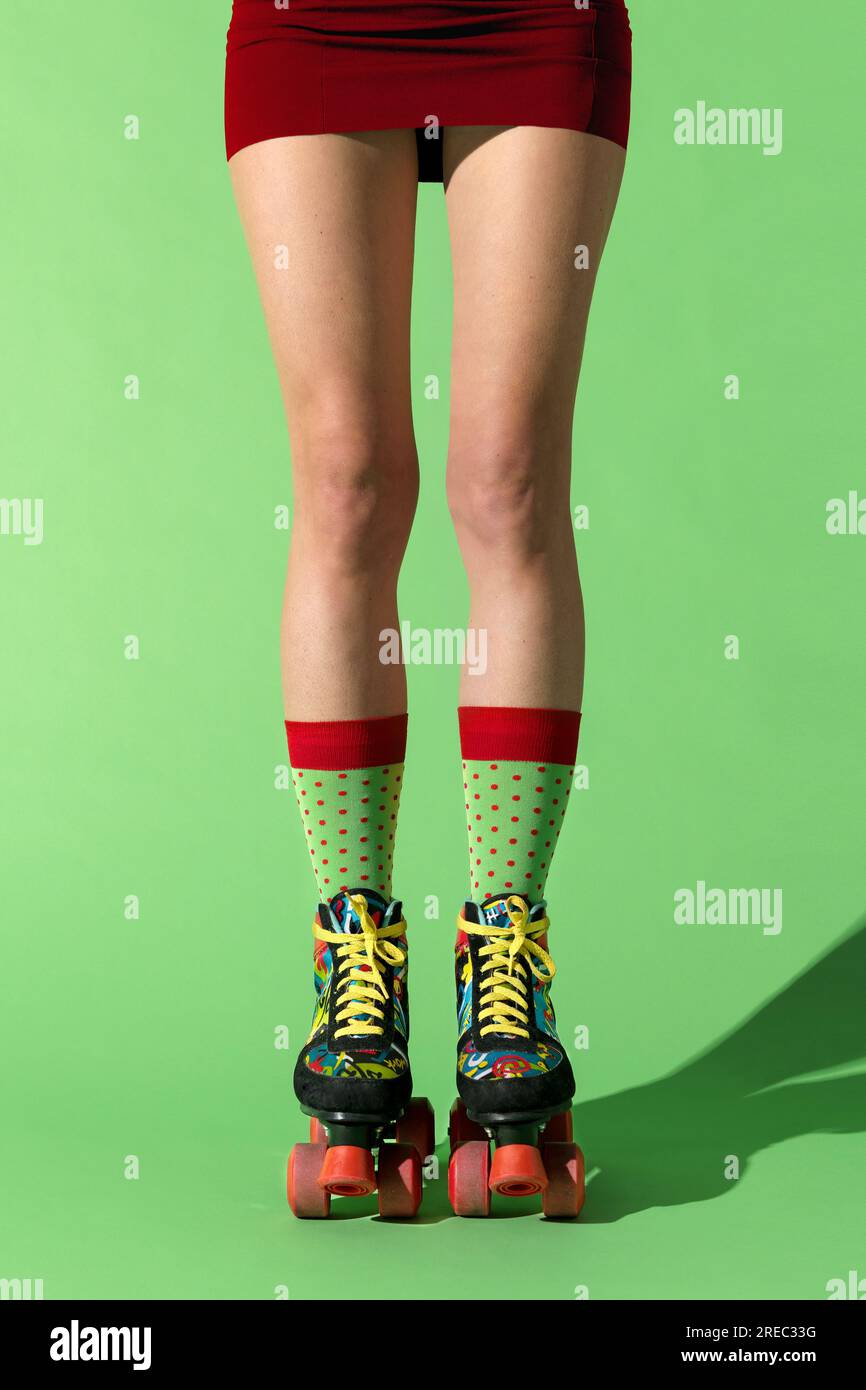 Nicht wiedererkennbare Millennials in Minirock-Socken und Rollschuhen vor grünem Hintergrund Stockfoto