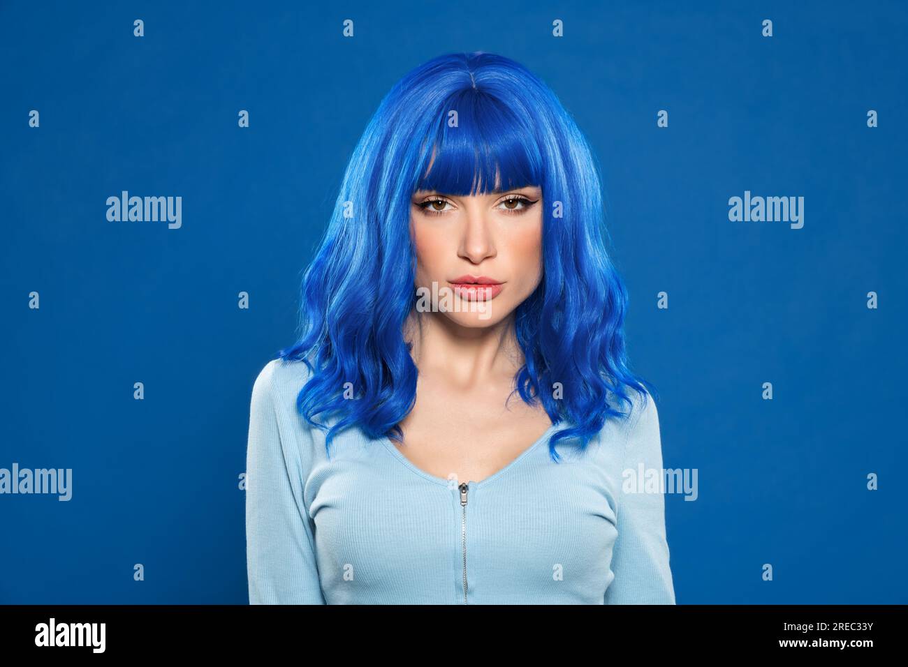 Porträtfoto einer Frau mit blauem Haar, die im Studio vor einem lebendigen Hintergrund in die Kamera schaut Stockfoto