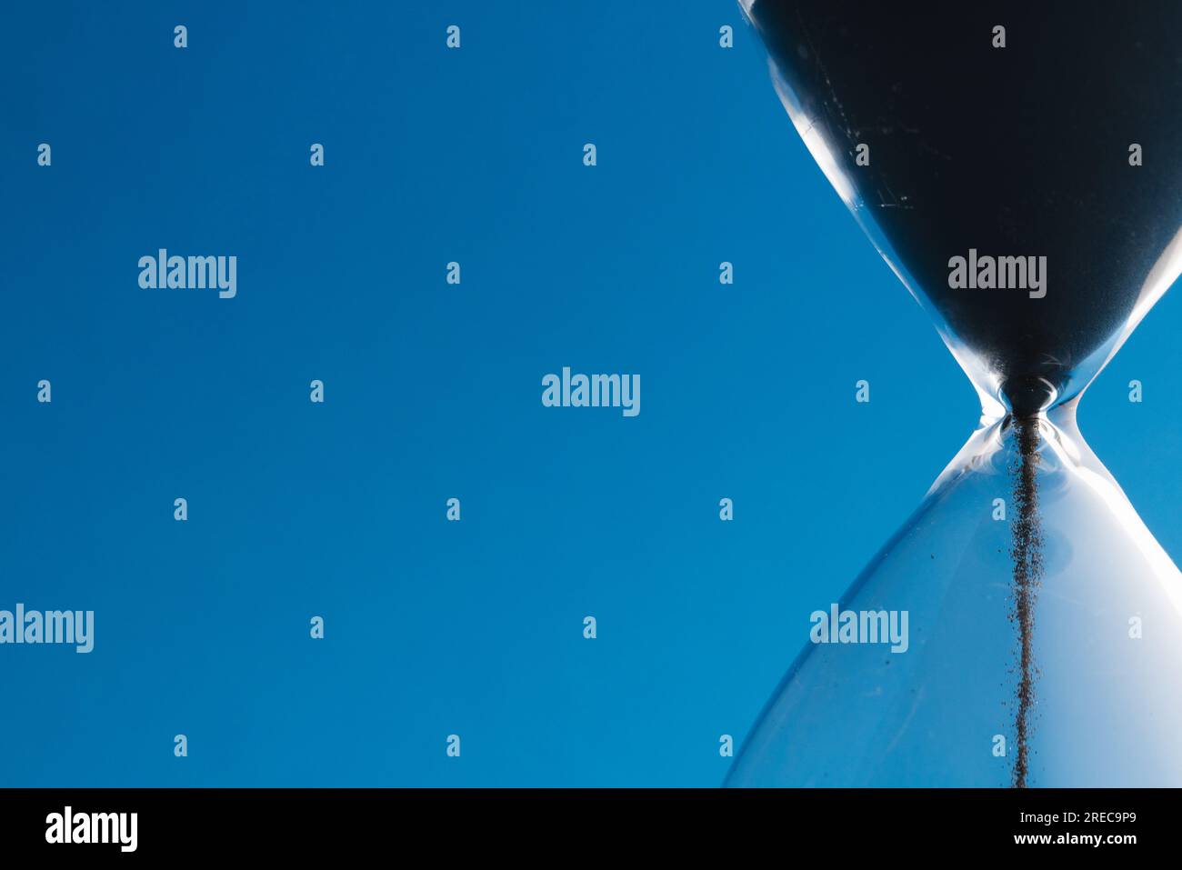 Nahaufnahme der Sanduhr mit schwarzem Sand und Kopierbereich auf blauem Hintergrund Stockfoto