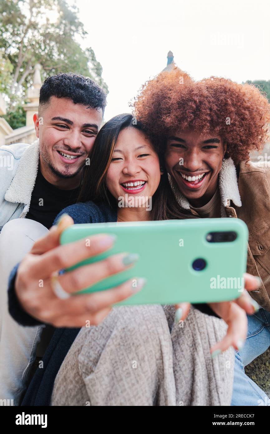 Vertikales Porträt einer Gruppe von multiethnischen Freunden im Teenageralter, die Spaß haben, ein Selfie mit einem Mobiltelefon zu machen. Junge, glückliche Menschen, die lächeln und lustige Videos ansehen oder ein Videogespräch mit einem Mobiltelefon führen. Hochwertiges Foto Stockfoto