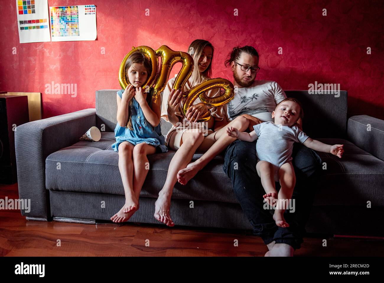 Ein kleines Mädchen mit weihnachtlicher Mütze steckte den Kopf in den Folienladen. Porträt einer glücklichen, vielfältigen Familie, die herumtreibt und Spaß für das jahrelange Baby hat. B Stockfoto