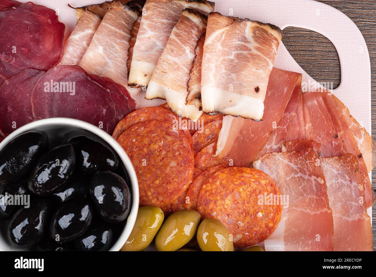 Blick von oben auf Speckscheiben, Prosciutto, Pastrami und Chorizo. Schwarze und grüne Oliven. Gute Vorspeisen für Wein oder Bier. Flach liegend, Nahaufnahme. Stockfoto
