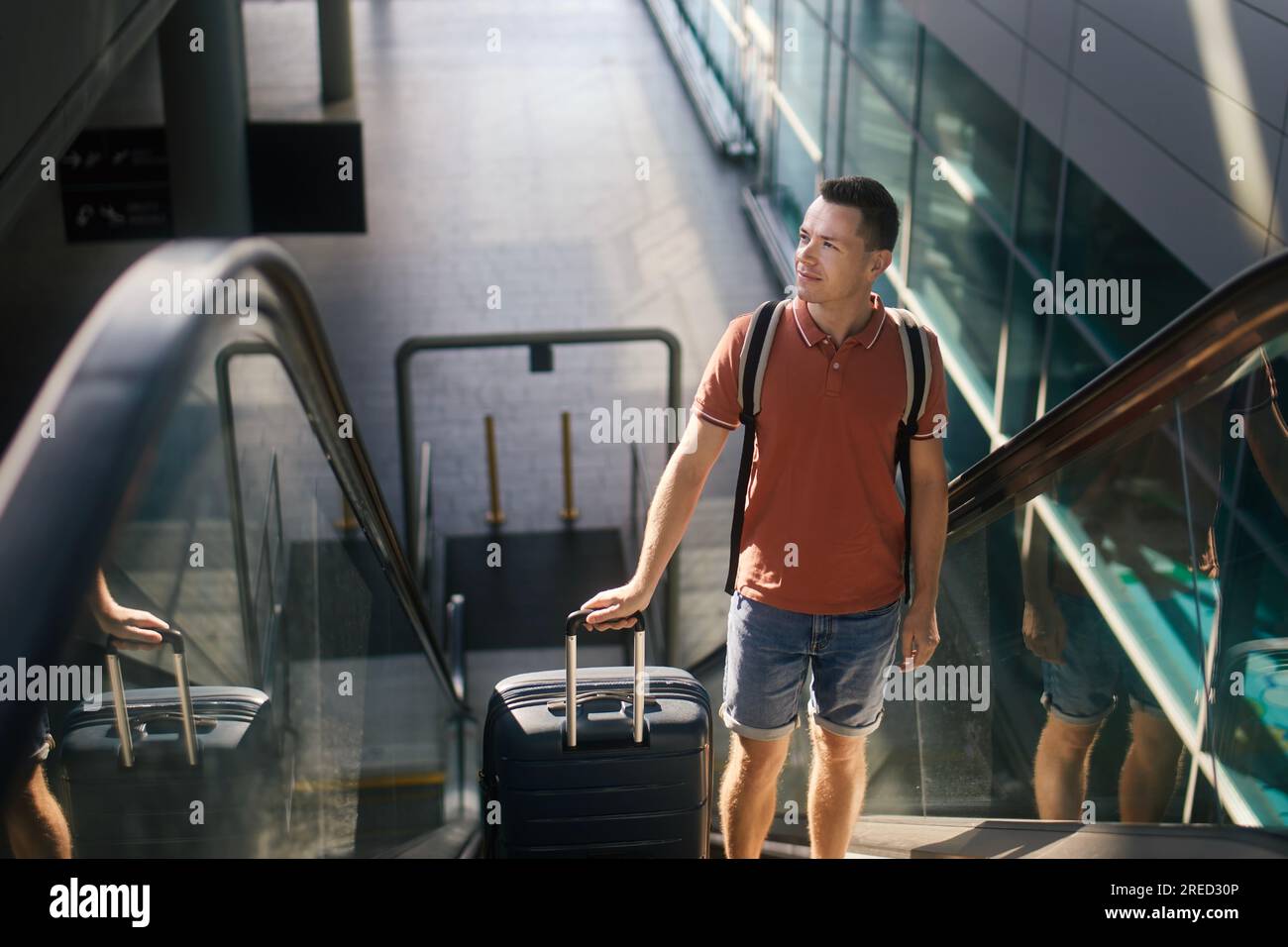 Reisende, die durch den Flughafenterminal laufen. Ein Mann mit Koffer steht auf dem Ekalator. Der Passagier ist bereit für die Reise mit dem Flugzeug. Stockfoto