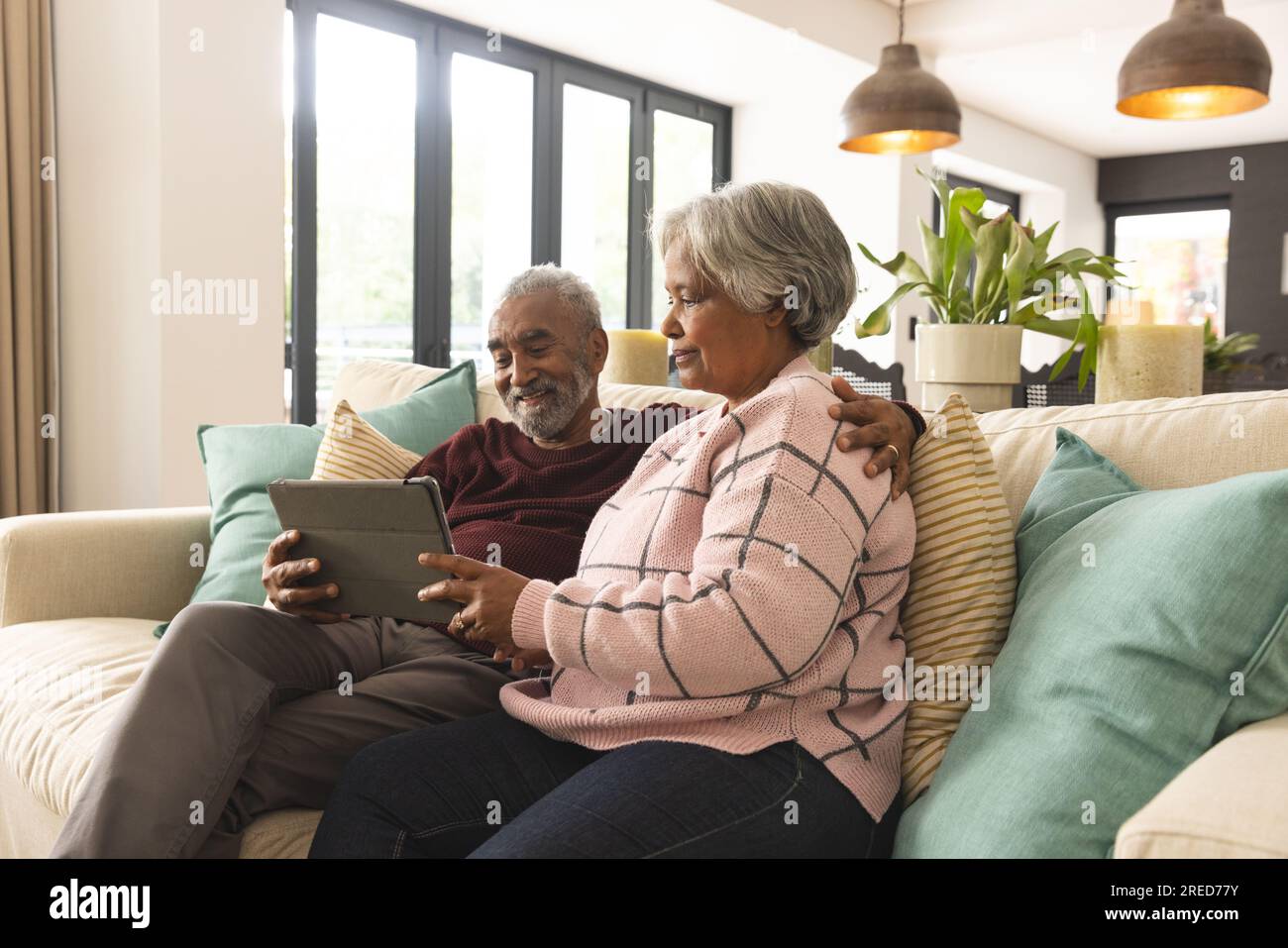 Glückliches älteres, birassisches Paar, das zu Hause auf dem Sofa sitzt und ein Tablet-Videogespräch führt Stockfoto
