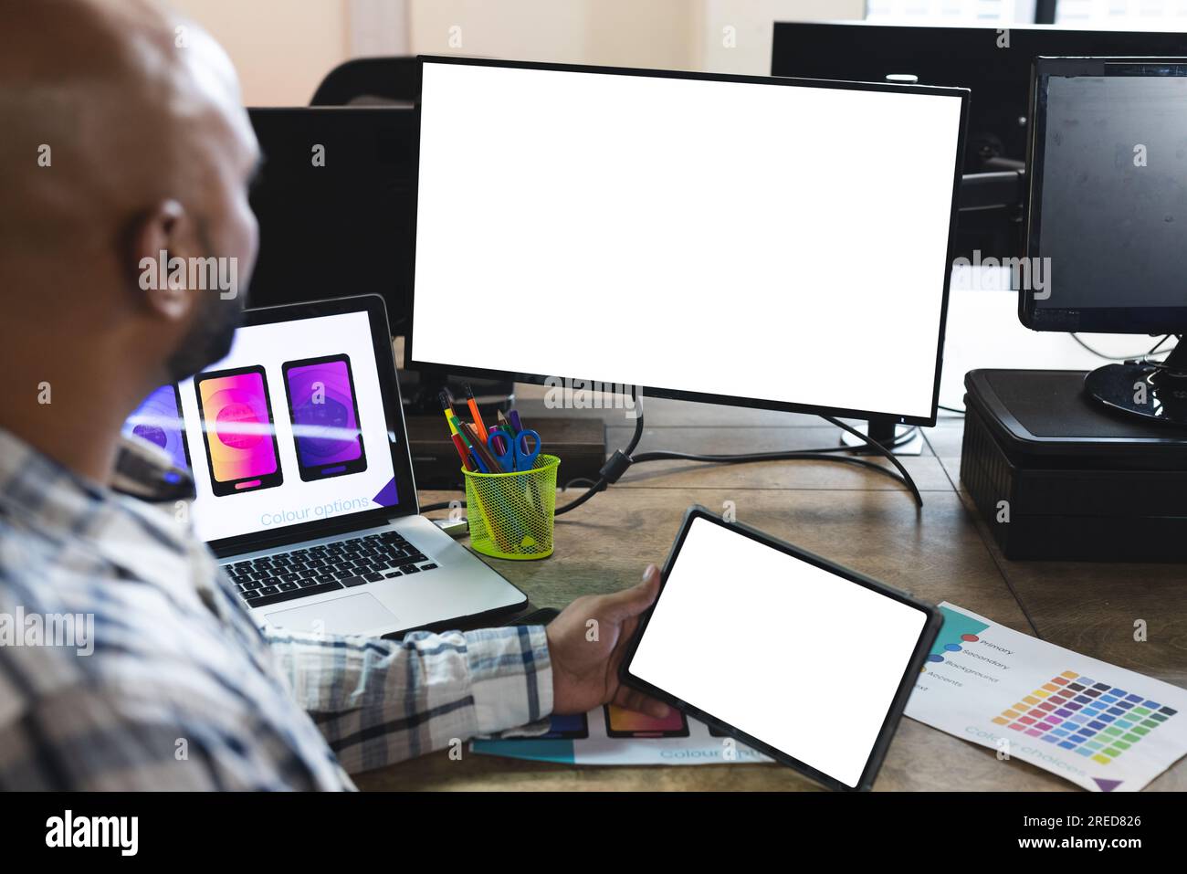 Indischer männlicher Designer, der Tablet und Computer mit Kopierbereich auf Bildschirmen am Schreibtisch im Büro benutzt Stockfoto
