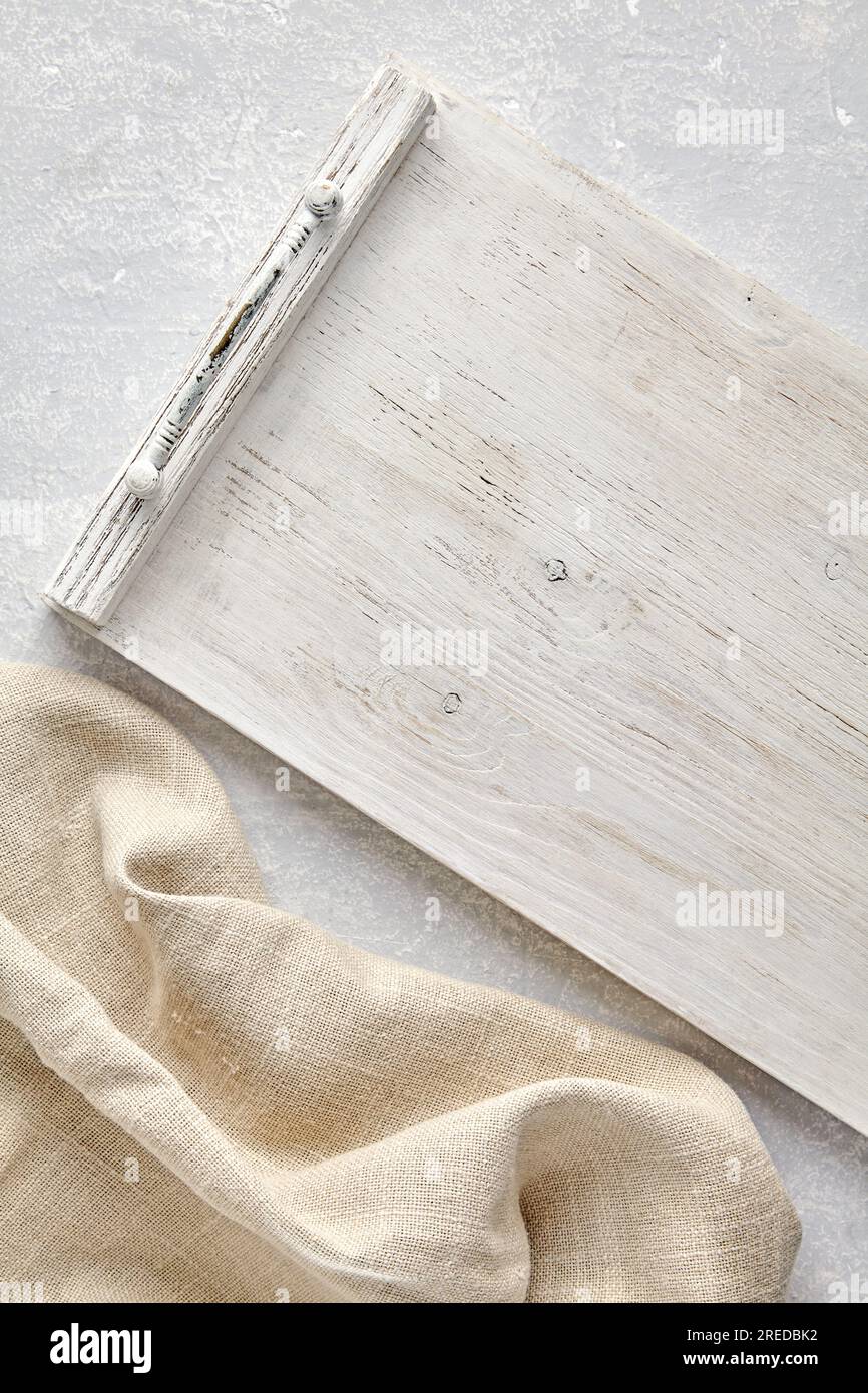 Weißes, aus Holz gestrichenes Serviertablett der Provence und grobe Bettwäsche Beige Küchentücher auf grauem Steintisch Blick von oben mit Kopierbereich Stockfoto