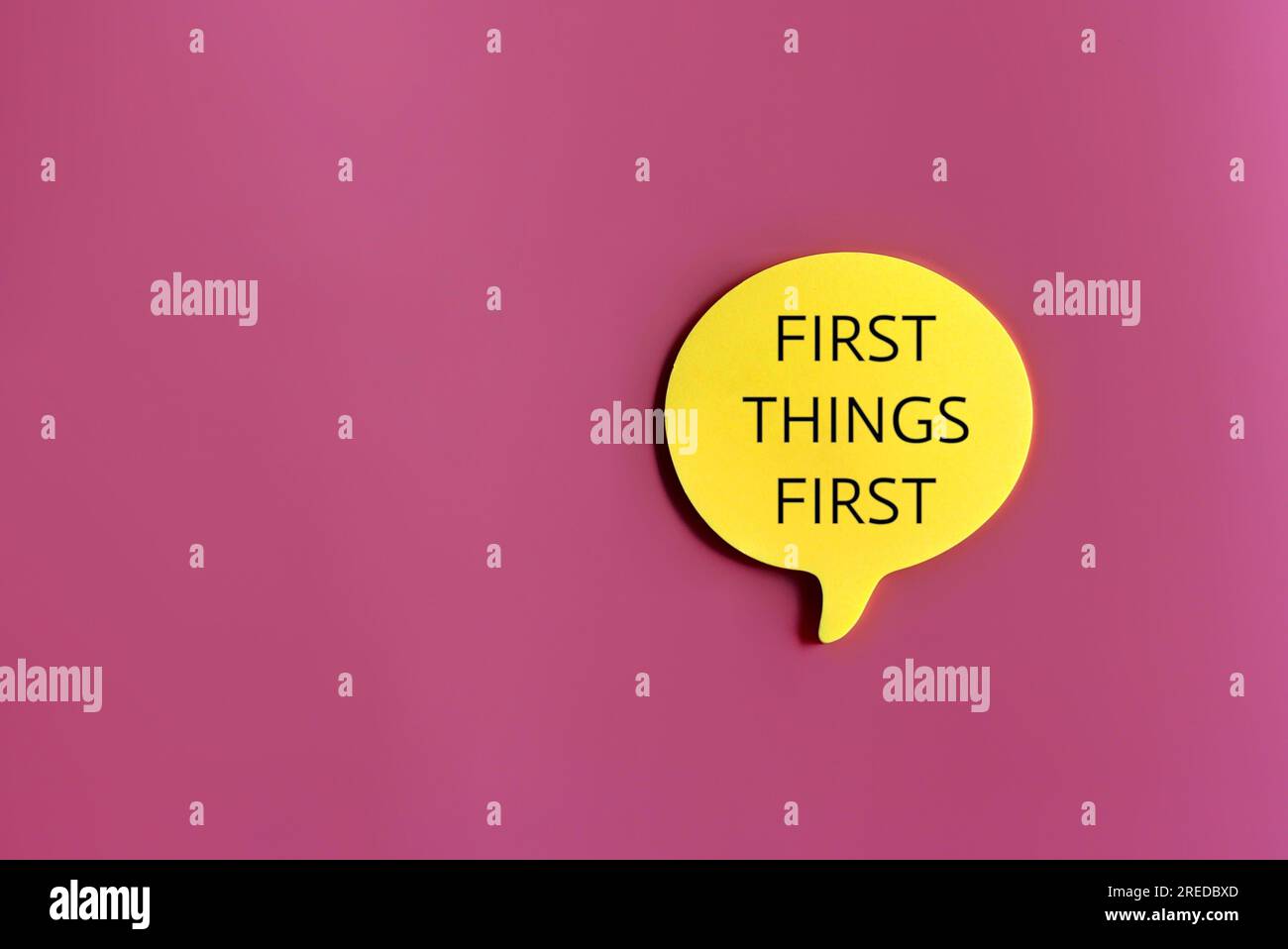 Bild der Sprechblase in der Draufsicht mit Text FIRST THINGS FIRST auf pinkfarbenem Hintergrund mit Kopierbereich Stockfoto