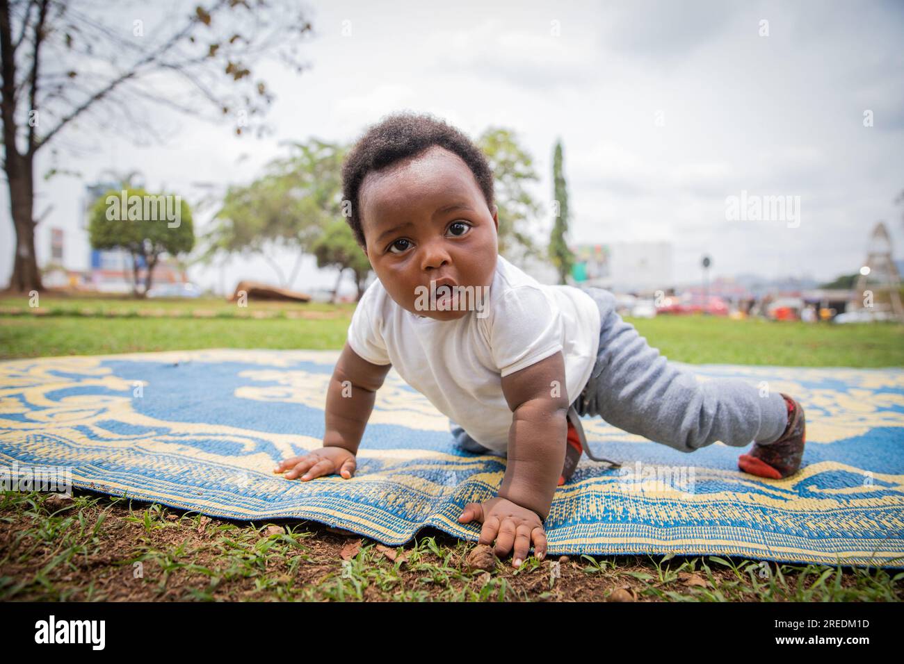 Ein afrikanisches Neugeborenes mit einem überraschten Look krabbelt auf einem Picknick-Tischtuch Stockfoto