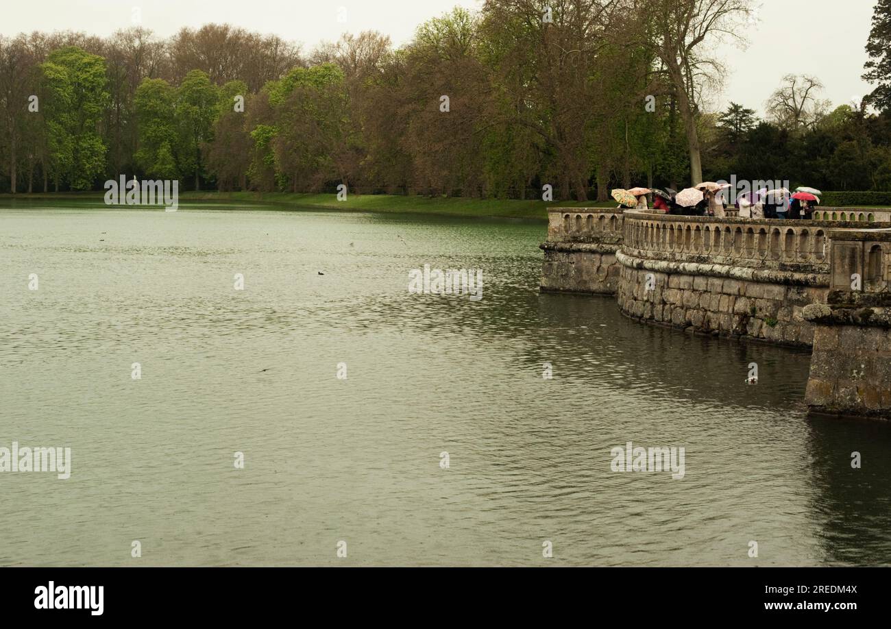 Im Palast Fontainebleau in der Nähe von Paris in Frankreich stehen viele Touristen unter Sonnenschirmen am Wasser Stockfoto