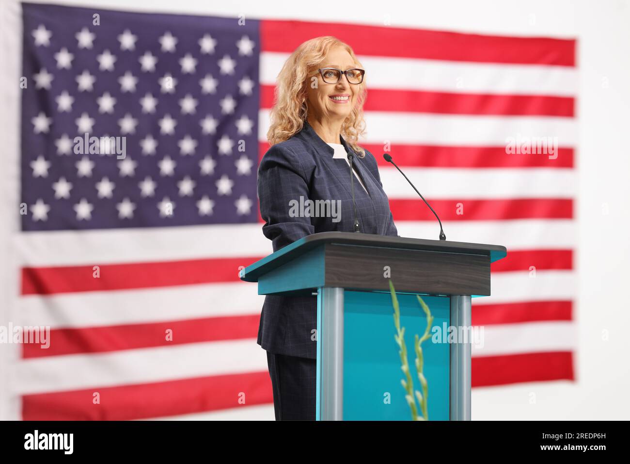 Eine weibliche Politikerin auf einem Lautsprecher steht mit der US-Flagge im Hintergrund Stockfoto