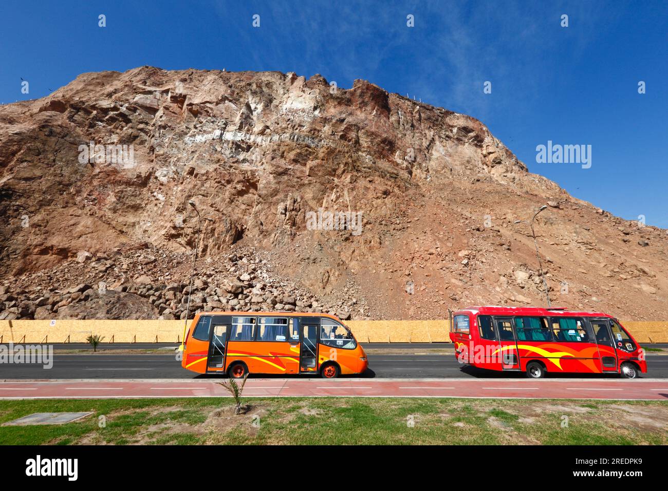 Rot-orange Busse mit öffentlichen Verkehrsmitteln auf der Av Costanera/Av. Comandante San Martín unterhalb der Klippen der Landzunge El Morro, Arica, Chile Stockfoto