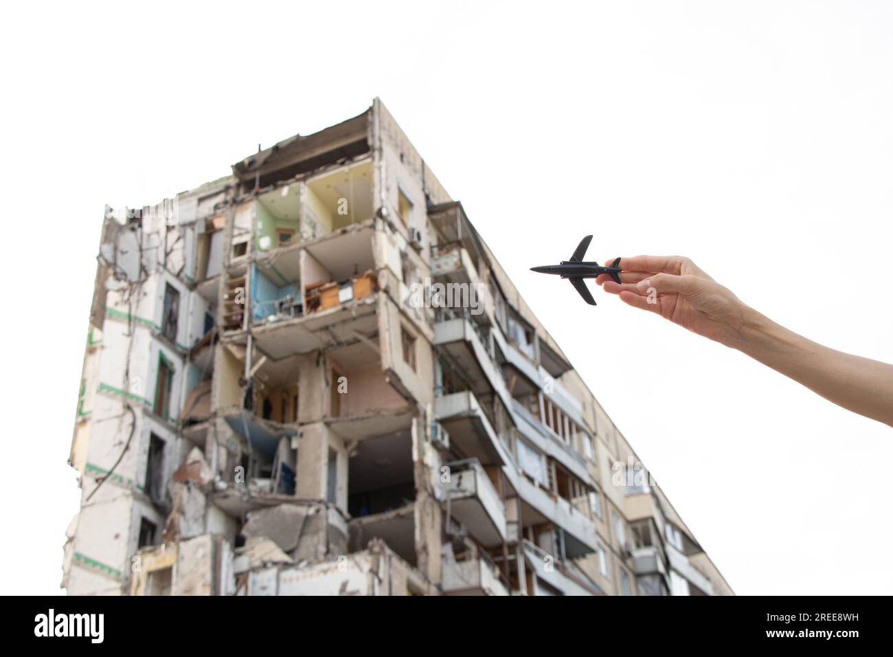 Die Hand einer Frau hält ein kleines Plastikflugzeug vor dem Hintergrund eines Hauses, das von einer russischen Rakete in die Luft gejagt wurde, im Dnjepr in der Ukraine, lassen Sie die Flugzeuge kl Stockfoto