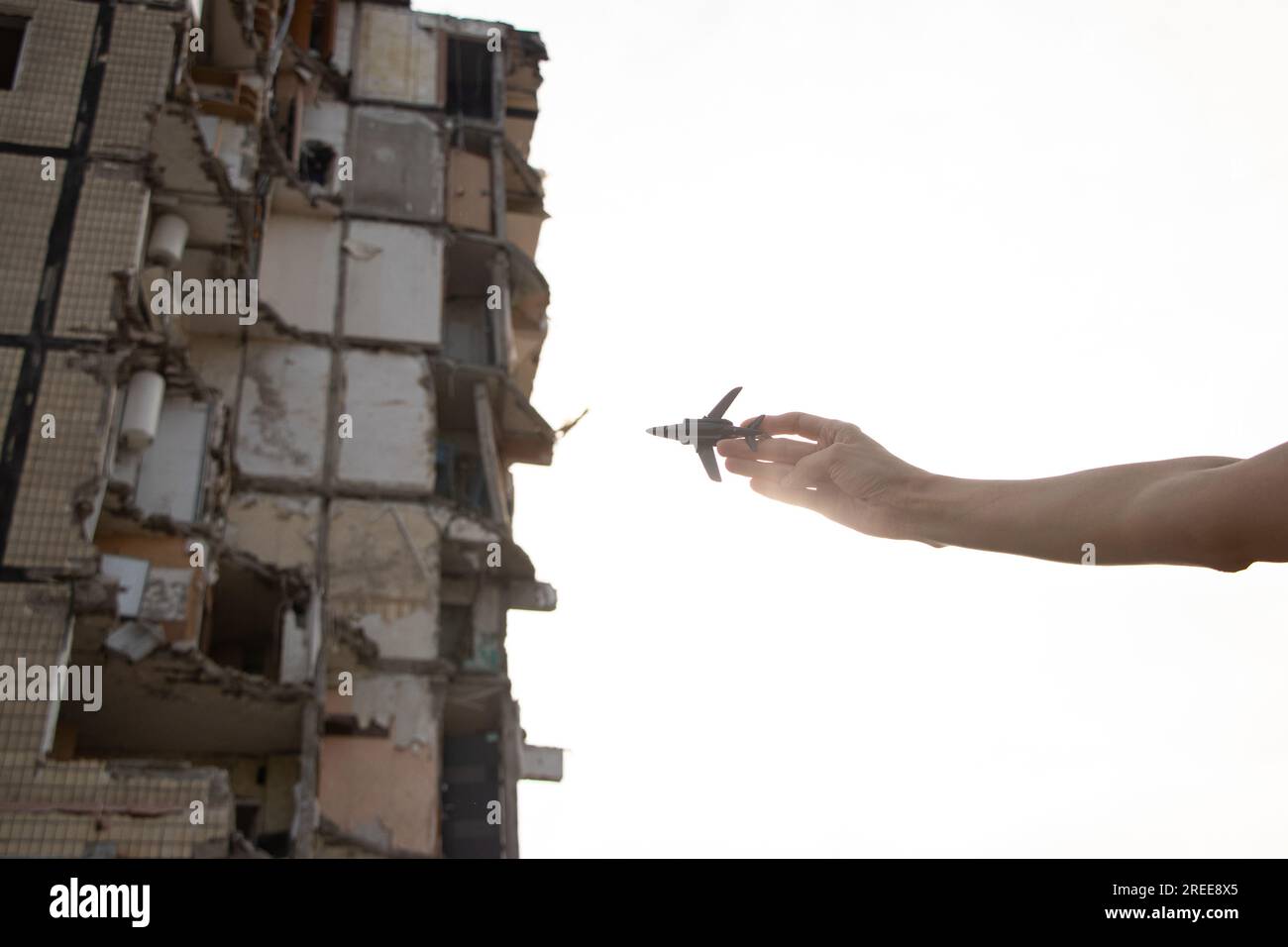 Die Hand einer Frau hält ein kleines Plastikflugzeug vor dem Hintergrund eines Hauses, das von einer russischen Rakete in die Luft gejagt wurde, im Dnjepr in der Ukraine, lassen Sie die Flugzeuge kl Stockfoto