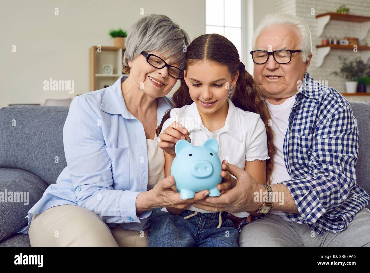 Glückliches kleines Mädchen, zusammen mit Oma und Opa, das Geld auf Sparschwein spart Stockfoto