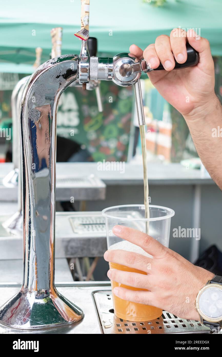 Ein Mann, der Bier in ein Plastikglas gießt, an einem Straßenstand. Sommerfestivals. Stockfoto