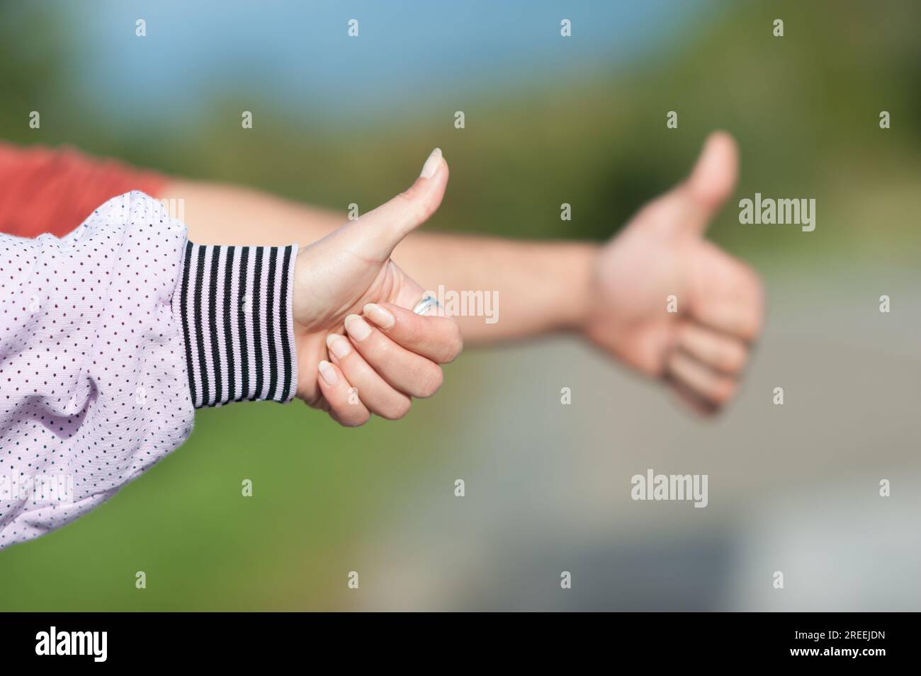 Detailansicht zweier Anhalter, weiblich und männlich, mit hochgezogenen Fingern, per Anhalter an einem sonnigen Tag. Autostop-Konzept Stockfoto