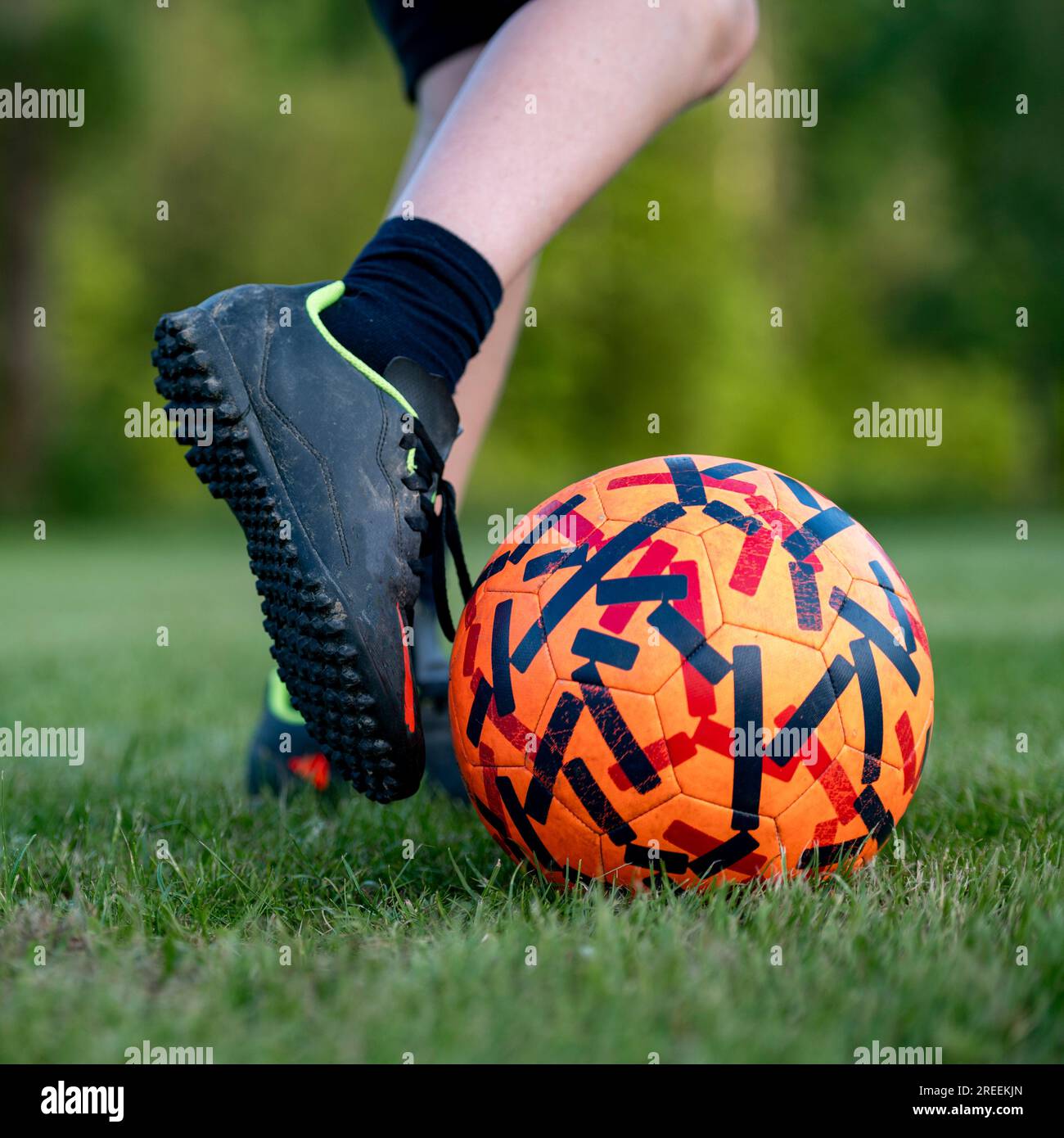 Nahaufnahme eines Fußes eines Teenagers, der beim Fußballtraining einen Fußball auf grünem Gras tritt. Stockfoto