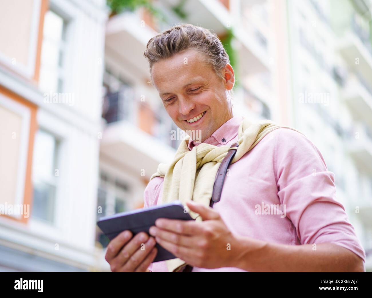Glücklicher Mann, der die neuesten Artikel über einen Tablet-PC liest, während er draußen auf der Straße ist. Mit dem Tablet-PC in seinen Händen kann er auf die neuesten Informationen zugreifen und sich über aktuelle Ereignisse auf dem Laufenden halten. . Hochwertiges Foto Stockfoto