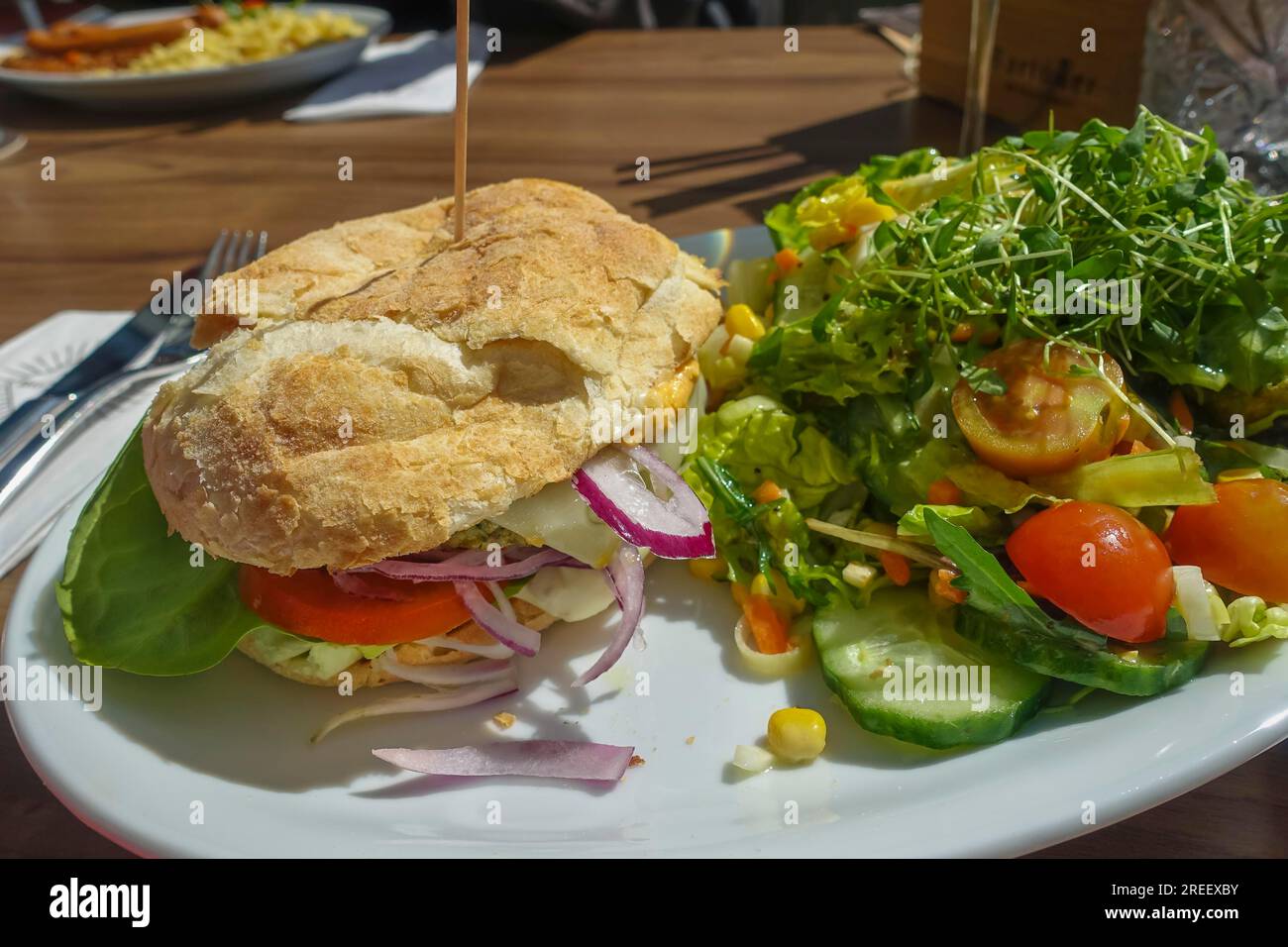 Vegetarische Küche, alpine Weidenburger, Burger auf Pflanzenbasis, Brötchen gefüllt mit Gemüse. Gesund, Salat, Tomaten, rote Zwiebeln, herzhaft, Gemüse Stockfoto