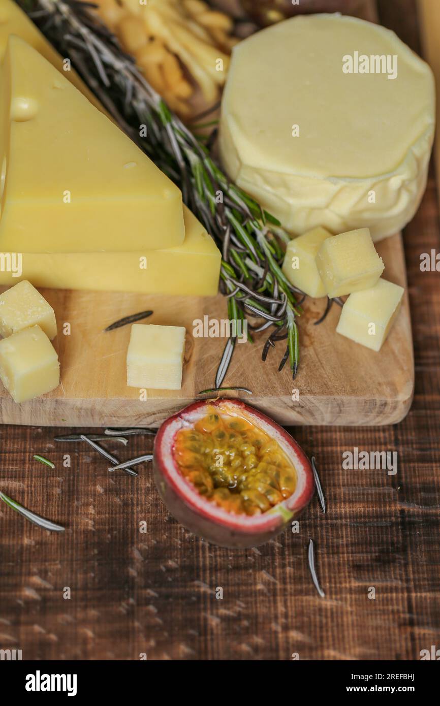 Käse auf einem Holzbrett mit Rosmarin und Passionsfrucht. Mazdar-Käse-Dreiecke, gouda-Käsewürfel, Chechil geräuchert Stockfoto