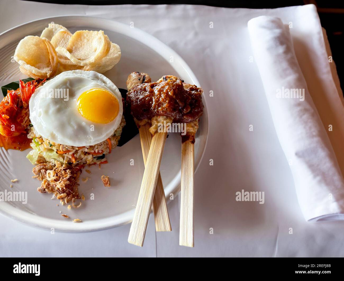 Gebratener indonesischer Reis Nasi Goreng serviert mit Sojasoße, Chilipasta, Sambal, sonniger Seite nach oben, Satay, Sate, Hühnerspieß und Kerupuk-Cracker Stockfoto