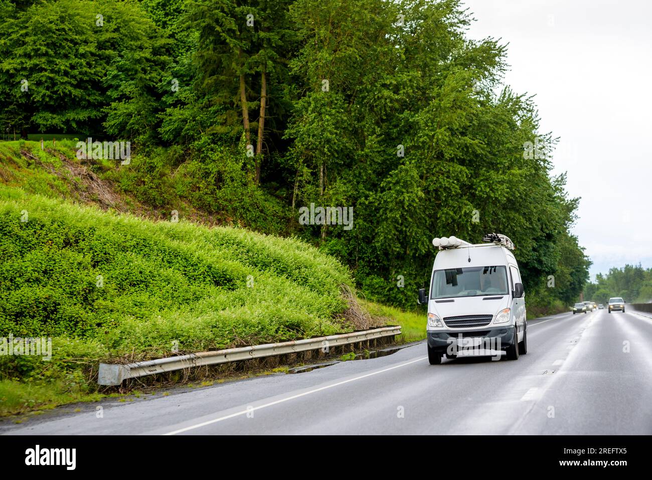 Weißer, kompakter, leicht manövrierbarer, sparsamer Kleinbus mit Rohren auf dem Dach, die auf nassen Autobahnen seitlich zur Wartung verlaufen Stockfoto