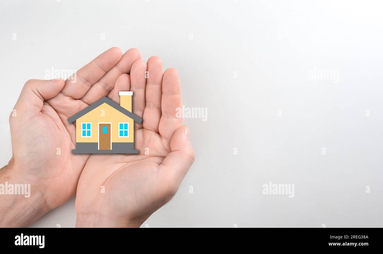 Nahaufnahme eines Hand- und Papierhausmodells vor weißem Hintergrund. Haus- und Hypothekenversicherung. Wohnungsbauhypothekenkrise Stockfoto