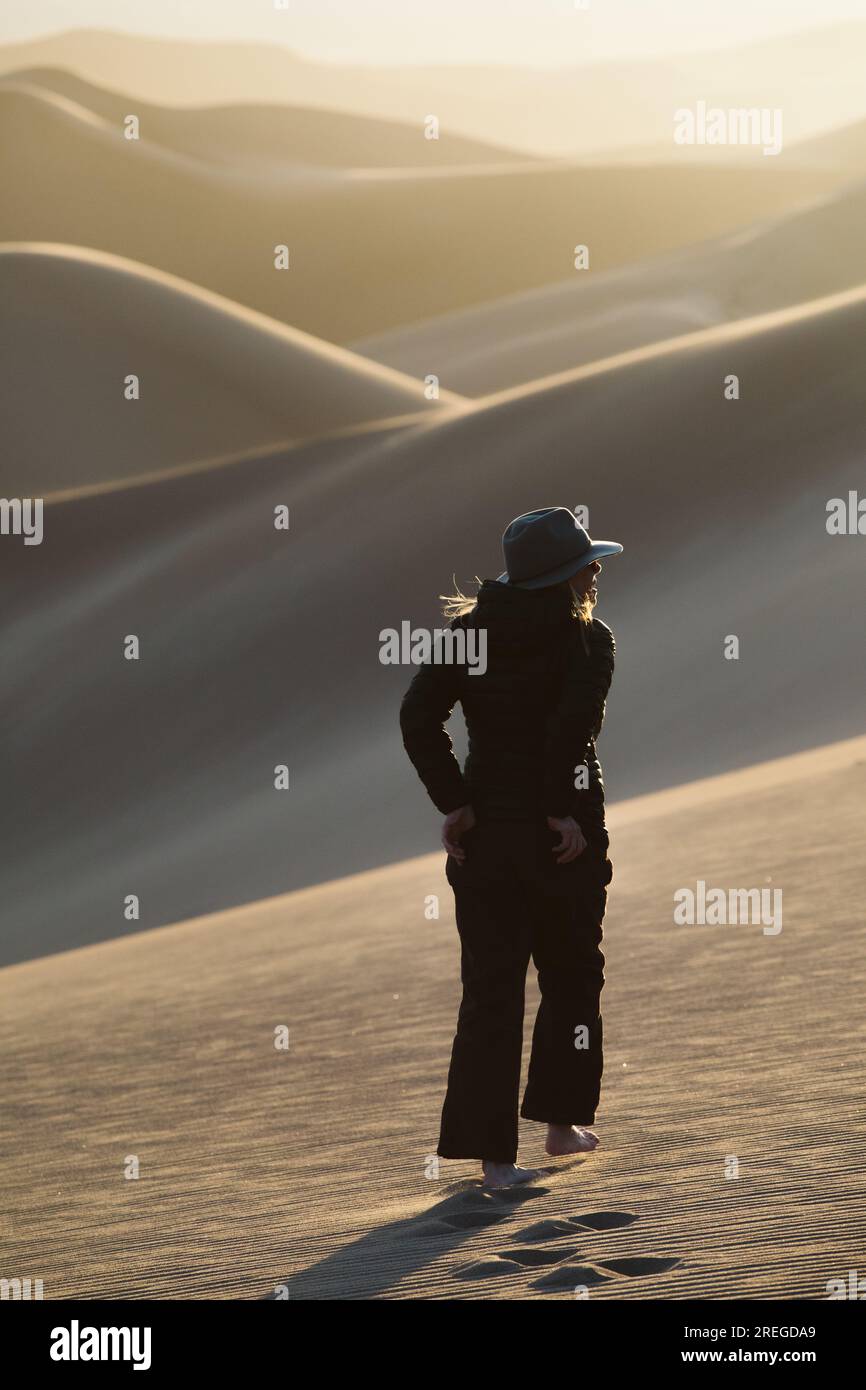 Eine alleinstehende Frau mit Filzhut und Händen in Hintertaschen wandert in Dünen Stockfoto