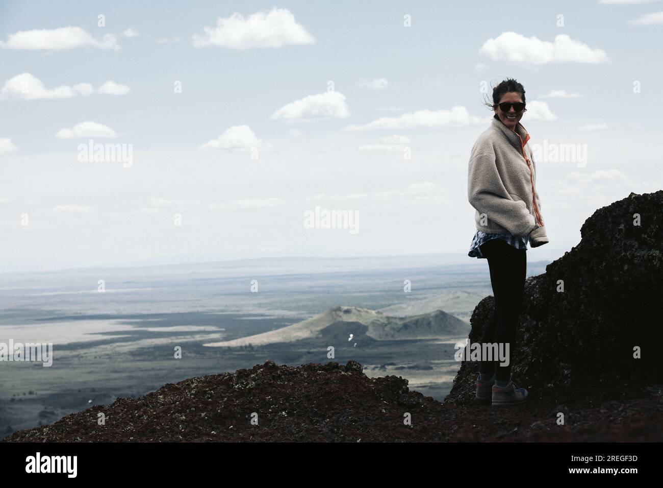 Eine Wanderin in Fleece lächelt vor der Kamera auf dem Gipfel eines bestimmten Vulkans Stockfoto
